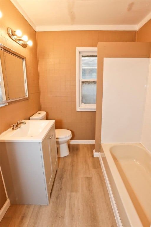 bathroom featuring toilet, hardwood / wood-style flooring, a bathtub, vanity, and ornamental molding