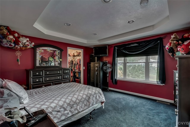 carpeted bedroom with a tray ceiling, a walk in closet, and a closet