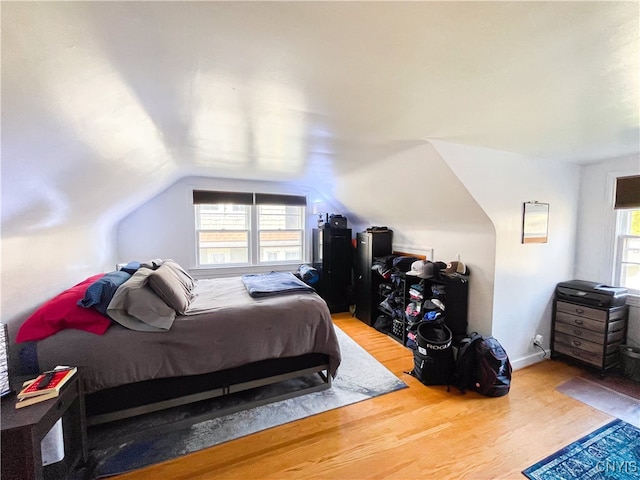 bedroom with light wood-type flooring, multiple windows, and lofted ceiling