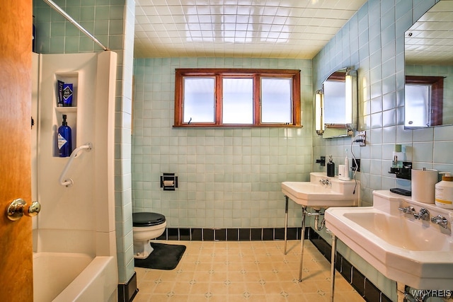 bathroom with tile walls, double sink, toilet, and bathtub / shower combination