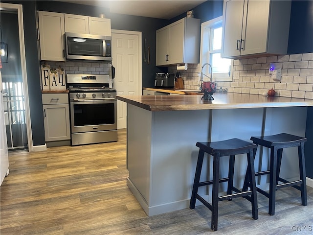 kitchen featuring stainless steel appliances, light wood-type flooring, decorative backsplash, a kitchen breakfast bar, and kitchen peninsula