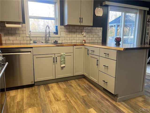 kitchen featuring stainless steel dishwasher, plenty of natural light, kitchen peninsula, and hardwood / wood-style floors