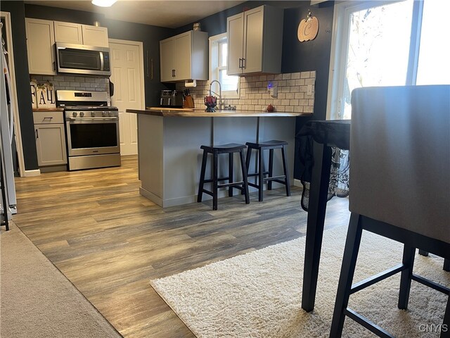 kitchen featuring light wood-type flooring, backsplash, appliances with stainless steel finishes, a breakfast bar, and kitchen peninsula