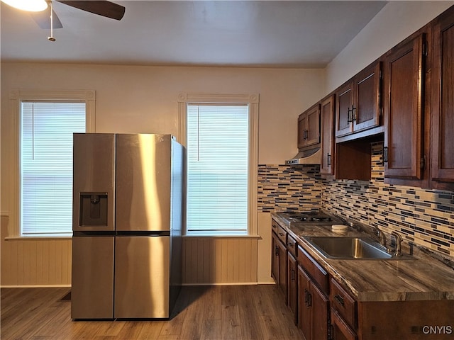 kitchen with wood walls, hardwood / wood-style flooring, sink, backsplash, and stainless steel fridge