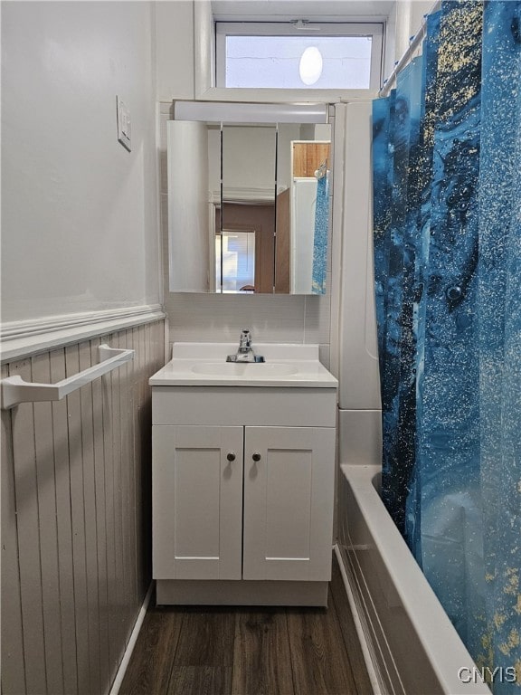 bathroom with hardwood / wood-style floors, wood walls, vanity, and shower / tub combo