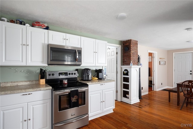 kitchen with light stone counters, stainless steel appliances, white cabinetry, a textured ceiling, and dark hardwood / wood-style flooring