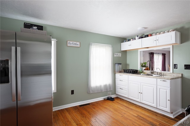 kitchen with white cabinetry, light hardwood / wood-style floors, a healthy amount of sunlight, and stainless steel fridge