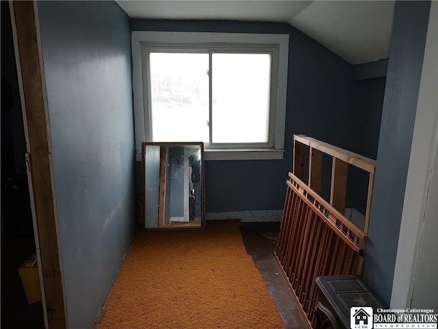 hallway with dark colored carpet and lofted ceiling