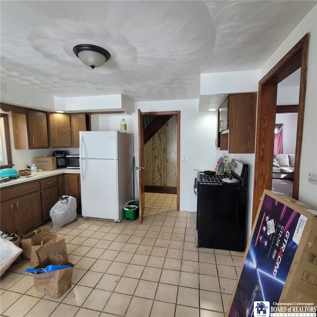 kitchen featuring light countertops, light tile patterned floors, gas stove, and freestanding refrigerator