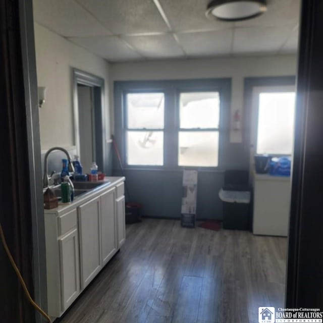 kitchen featuring a sink, wood finished floors, white cabinets, light countertops, and a paneled ceiling