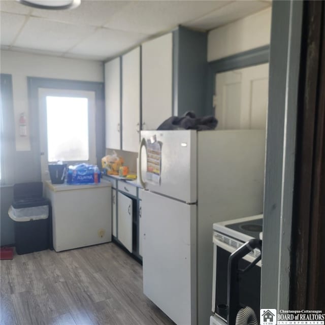 kitchen with wood finished floors, light countertops, white cabinets, a paneled ceiling, and white electric range