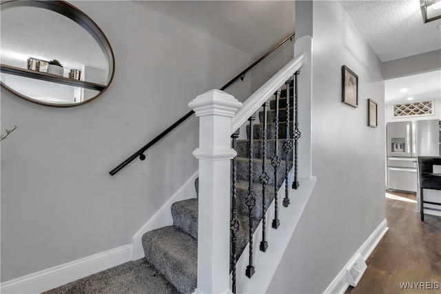 stairway with a textured ceiling and wood-type flooring