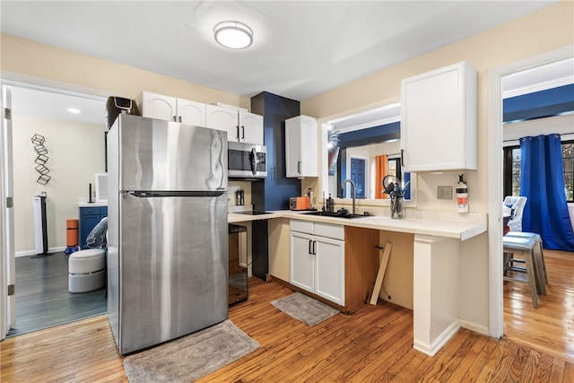 kitchen featuring white cabinets, stainless steel appliances, sink, and light hardwood / wood-style flooring