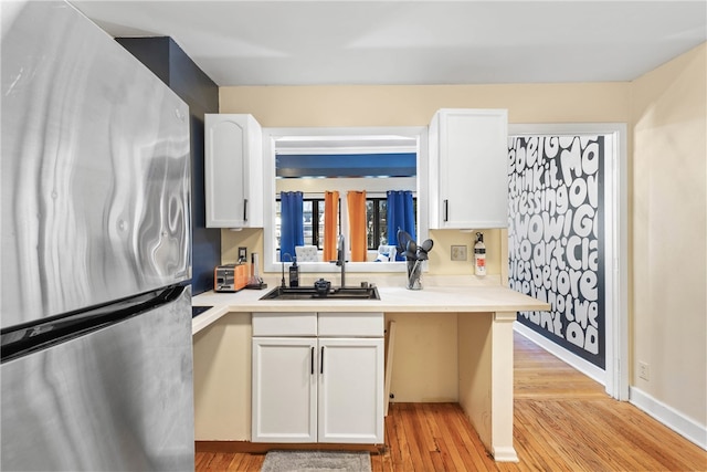 kitchen featuring white cabinetry, sink, stainless steel refrigerator, and light hardwood / wood-style flooring