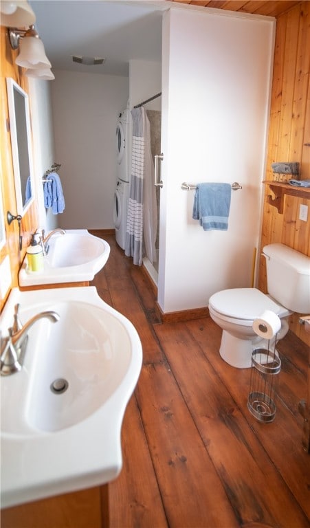 bathroom featuring stacked washer and dryer, wood walls, toilet, and a shower with curtain