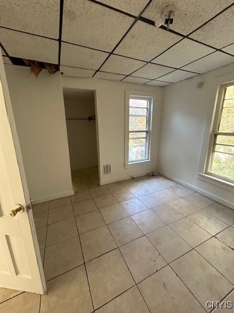 unfurnished bedroom featuring light tile patterned flooring, a paneled ceiling, a closet, and a walk in closet