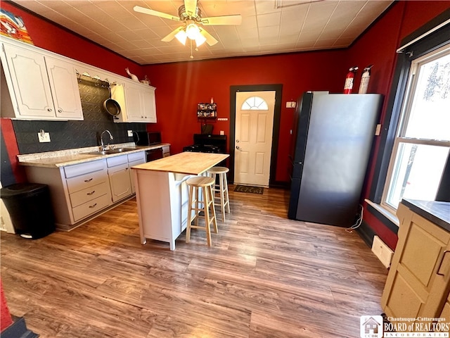 kitchen with black appliances, butcher block countertops, a kitchen bar, light hardwood / wood-style floors, and a center island