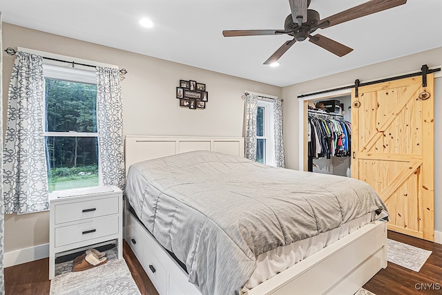 bedroom featuring a barn door, ceiling fan, a closet, and dark hardwood / wood-style flooring