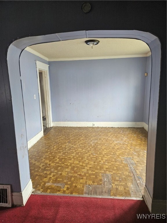 spare room featuring wooden walls, parquet flooring, and crown molding