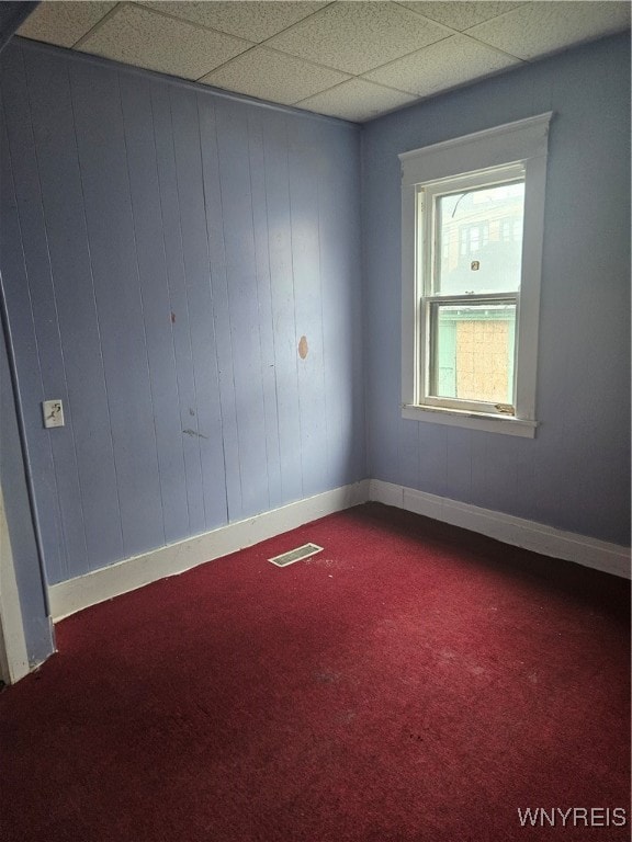 carpeted spare room featuring wooden walls and a drop ceiling