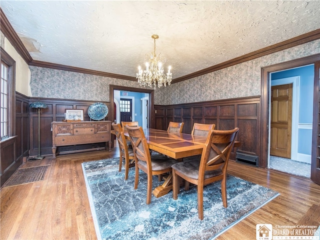 dining room featuring ornamental molding, wood-type flooring, a textured ceiling, and an inviting chandelier