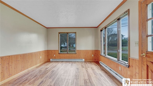 empty room featuring wood walls, light wood-type flooring, ornamental molding, and a baseboard heating unit