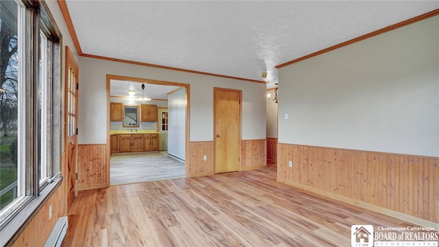 spare room featuring wood walls, a baseboard heating unit, light hardwood / wood-style flooring, and crown molding