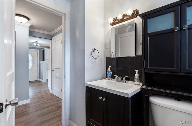 bathroom with wood-type flooring, ornamental molding, backsplash, vanity, and toilet