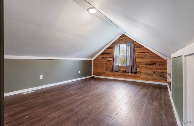 bonus room featuring dark wood-type flooring, wooden walls, and vaulted ceiling