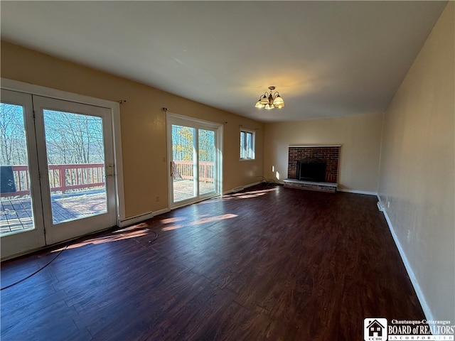 unfurnished living room featuring dark wood-type flooring, an inviting chandelier, baseboard heating, and a fireplace