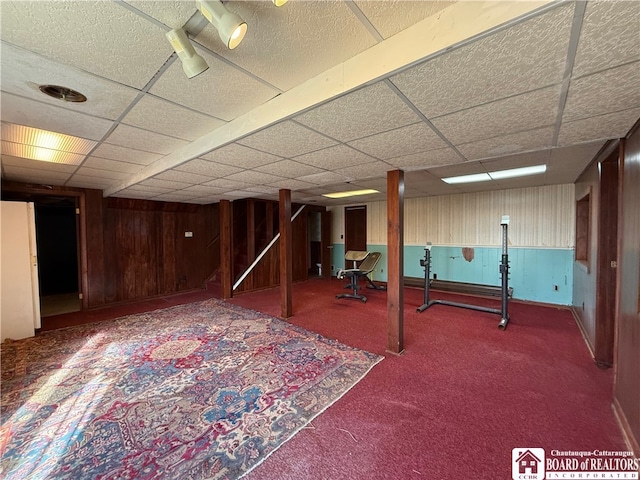 basement featuring carpet flooring, a paneled ceiling, and wood walls