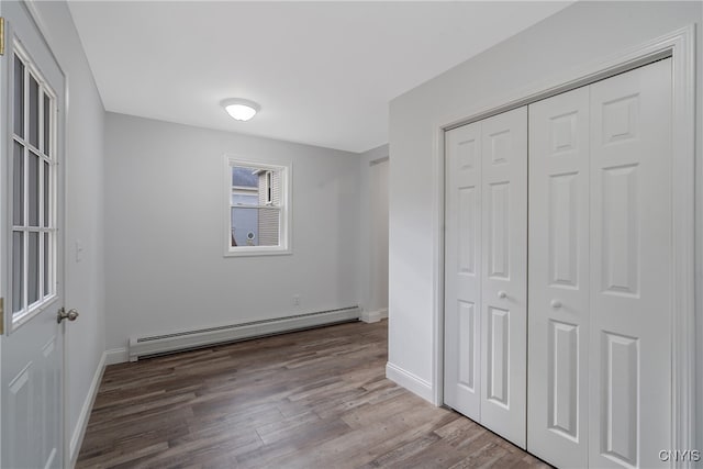 unfurnished bedroom featuring hardwood / wood-style flooring, a closet, and a baseboard heating unit