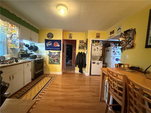 kitchen featuring stacked washing maching and dryer, white refrigerator, white cabinets, light hardwood / wood-style floors, and black range oven