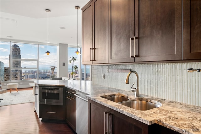 kitchen featuring sink, light stone counters, hanging light fixtures, dark wood-type flooring, and stainless steel oven