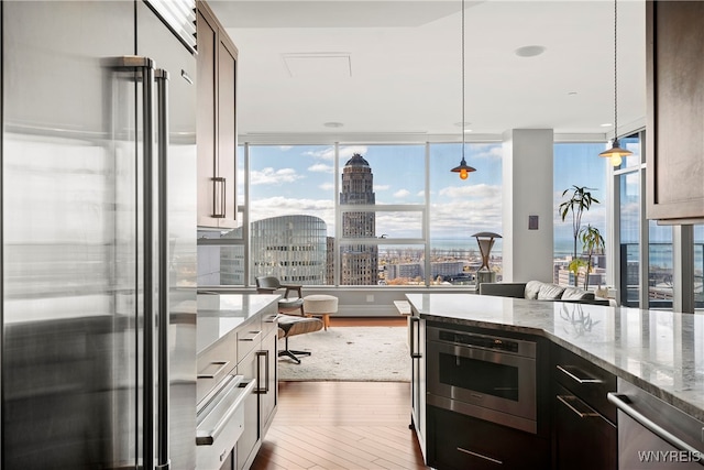 kitchen with wood-type flooring, floor to ceiling windows, light stone countertops, pendant lighting, and appliances with stainless steel finishes