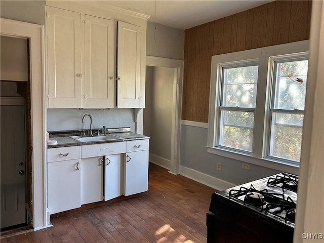 kitchen featuring black range with gas stovetop, sink, white cabinets, dark hardwood / wood-style floors, and wood walls