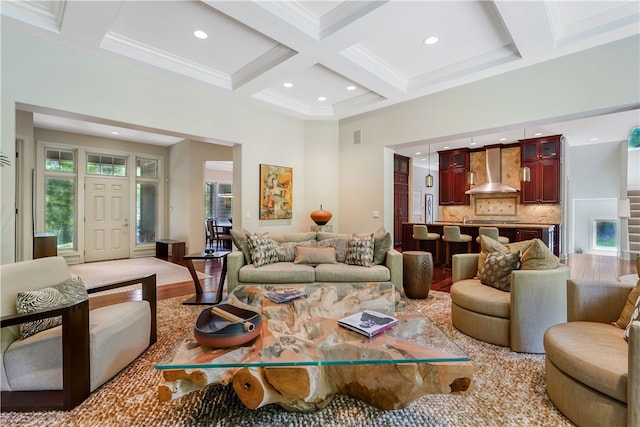 living room featuring beamed ceiling, coffered ceiling, ornamental molding, and light wood-type flooring