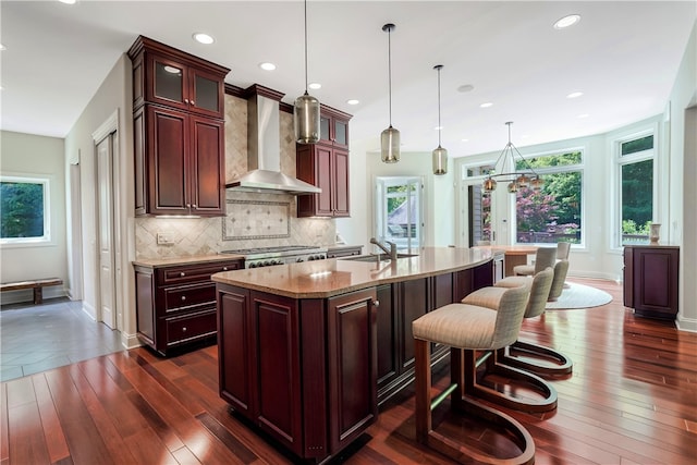 kitchen featuring wall chimney exhaust hood, tasteful backsplash, a kitchen island with sink, dark hardwood / wood-style floors, and pendant lighting