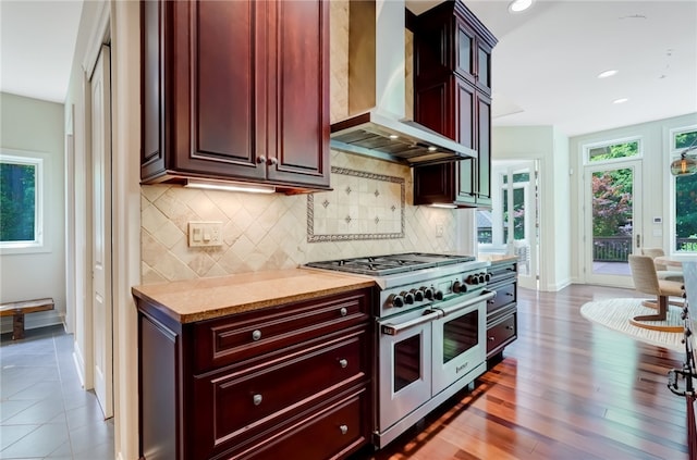 kitchen with wall chimney range hood, decorative backsplash, range with two ovens, and dark hardwood / wood-style floors