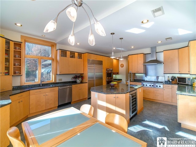 kitchen featuring wine cooler, appliances with stainless steel finishes, hanging light fixtures, wall chimney exhaust hood, and a kitchen island with sink