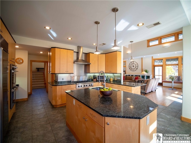 kitchen with a center island with sink, sink, kitchen peninsula, wall chimney exhaust hood, and decorative light fixtures