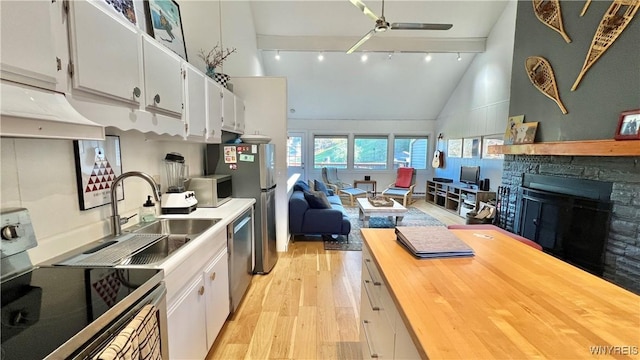 kitchen with open floor plan, stainless steel appliances, a stone fireplace, light wood-type flooring, and white cabinetry