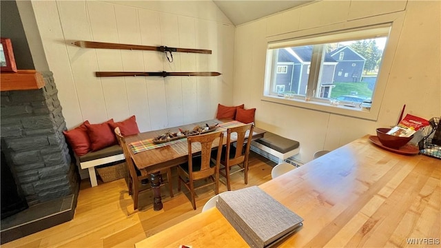 dining room with breakfast area, vaulted ceiling, a stone fireplace, and wood finished floors