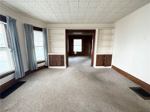 spare room featuring built in features, carpet floors, and a healthy amount of sunlight