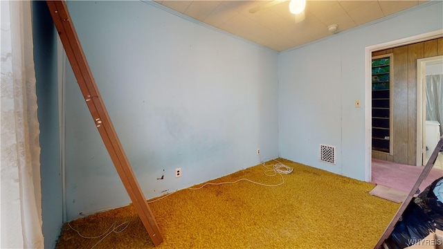 carpeted spare room featuring wood walls, ceiling fan, and crown molding