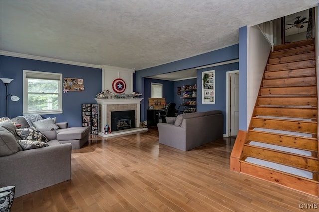 living room featuring light wood-type flooring, a textured ceiling, a tile fireplace, and crown molding