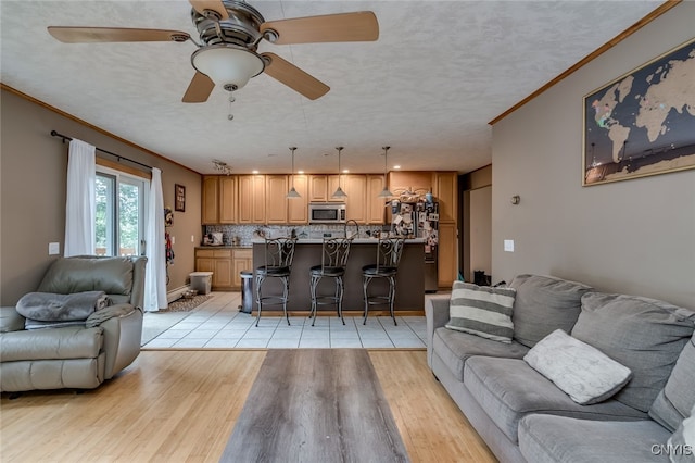 living room featuring ceiling fan, a textured ceiling, light wood-type flooring, and crown molding