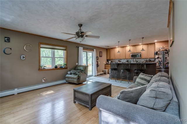 living room with light hardwood / wood-style floors, ceiling fan, a baseboard radiator, and a textured ceiling