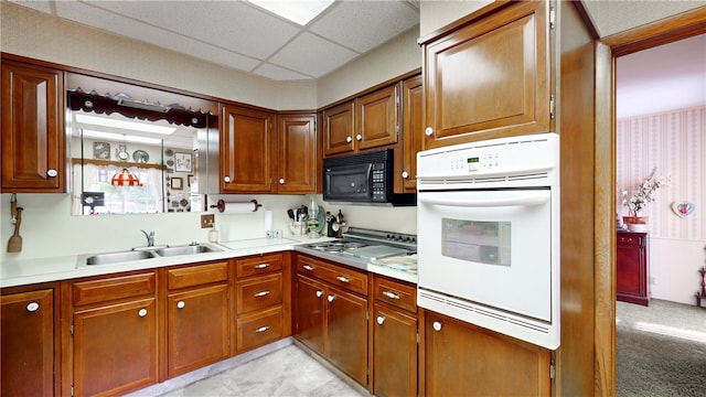 kitchen featuring sink, stainless steel gas stovetop, a paneled ceiling, light colored carpet, and oven