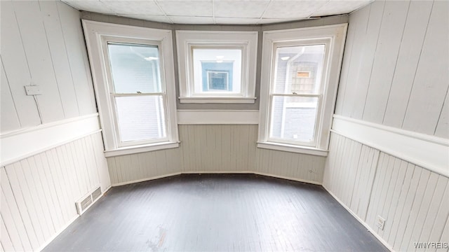 empty room with wooden walls, dark hardwood / wood-style floors, and a healthy amount of sunlight